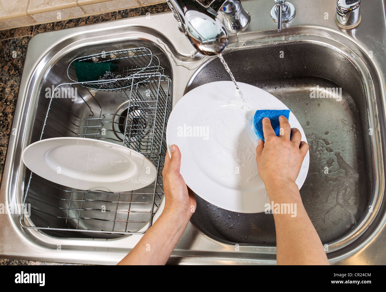 Hands washing dishes with running water from faucet in sink Stock Photo