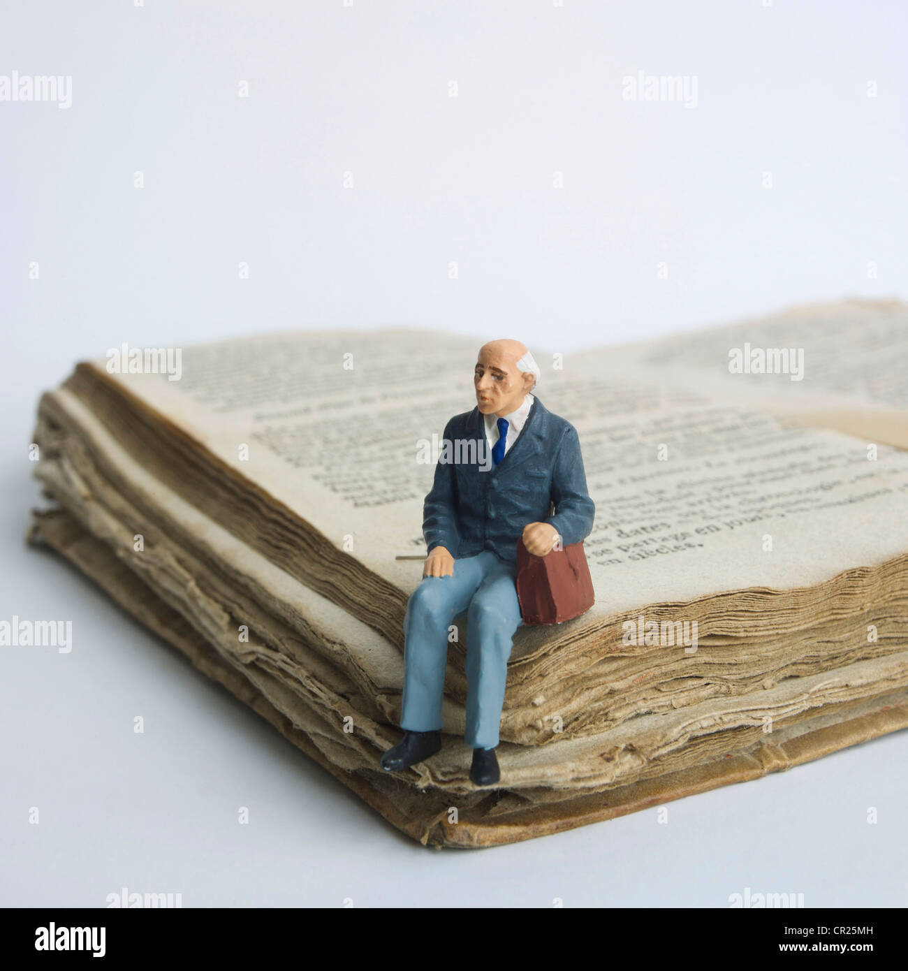 Elderly man, miniature figurine, sitting on an old book. Stock Photo