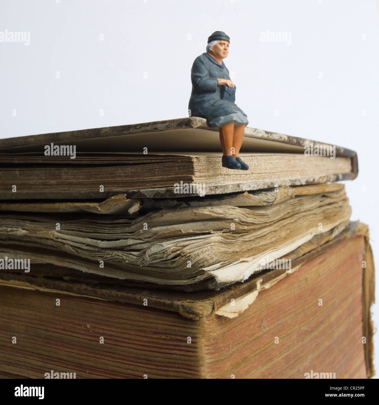 Elderly lady, miniature figurine, sitting on an old book - knowledge / wisdom / life history concept. Stock Photo