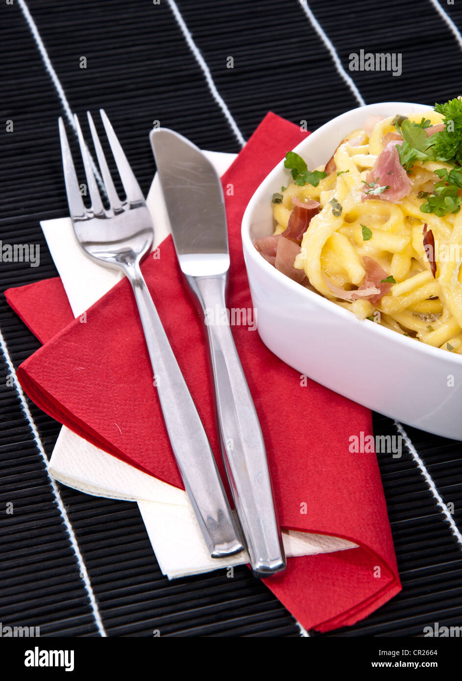 Cheese Spaetzle decorated with herbs and cutlery (on black background