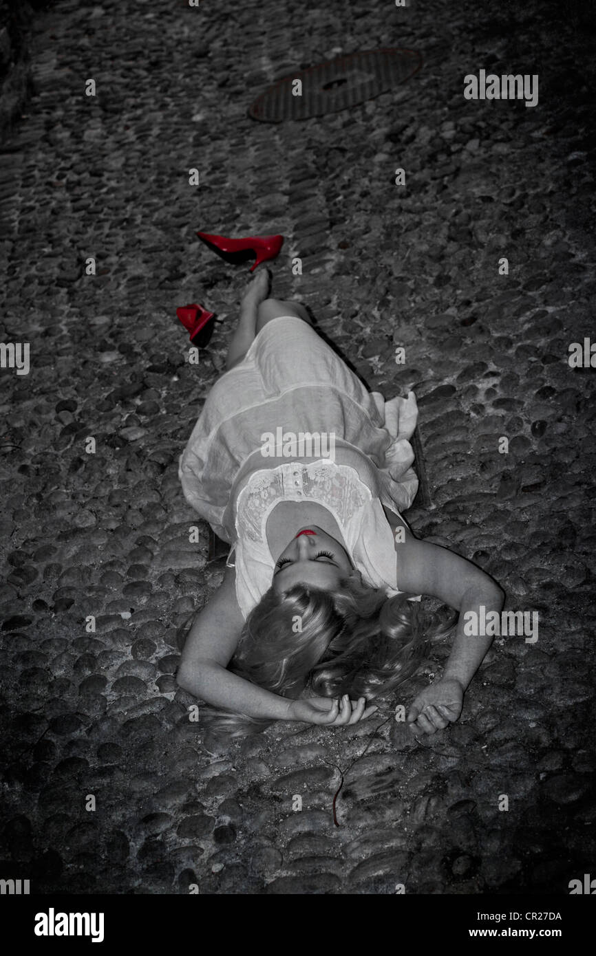 young woman lying on the street on a cobblestone in a white dress with red pumps Stock Photo