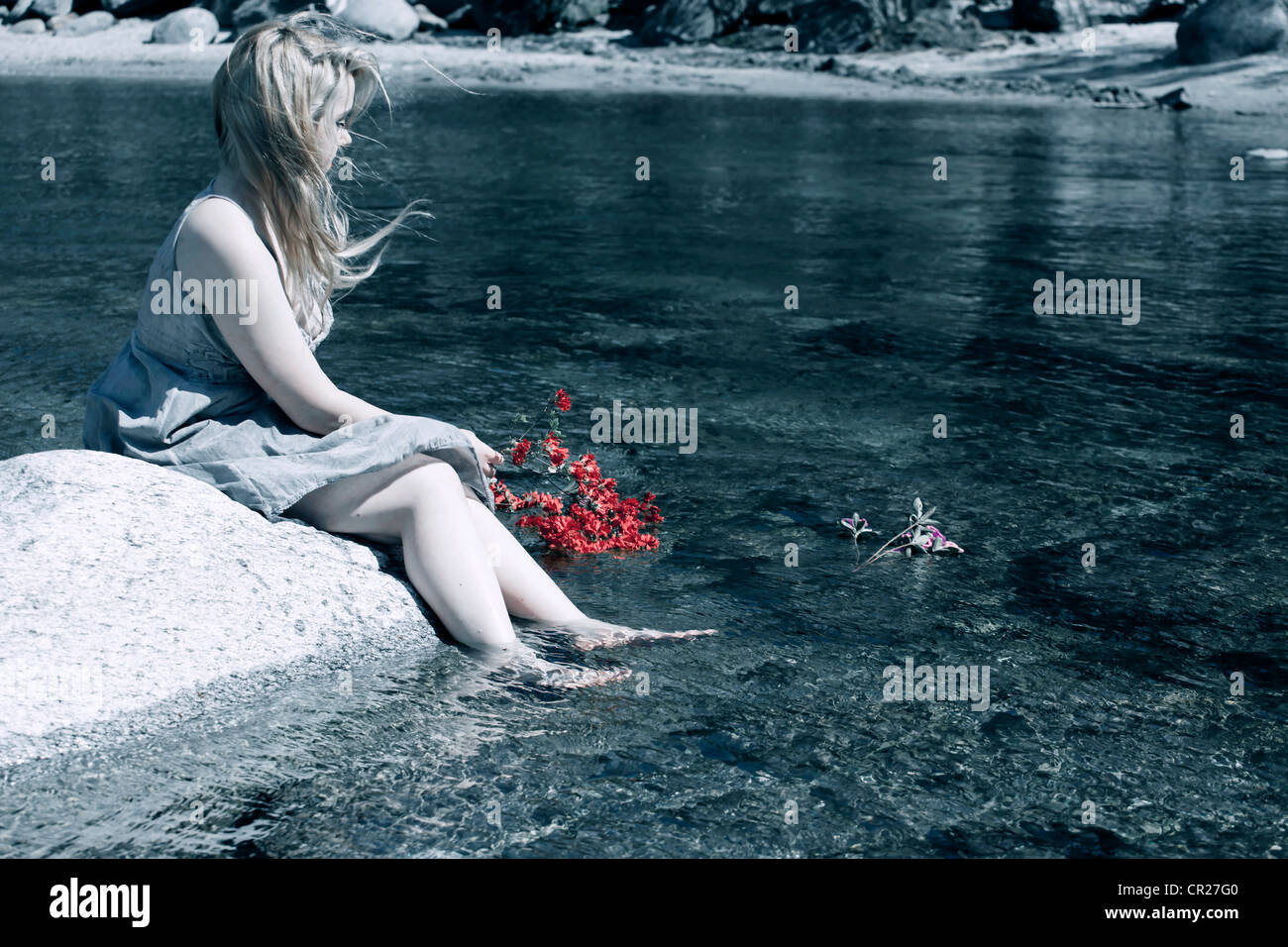 young woman on a rock surrounded by a mountain stream, she throws flowers into the water Stock Photo