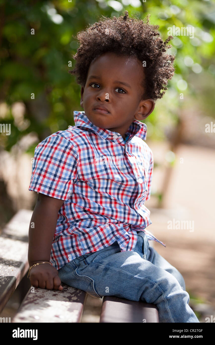 Outdoor portrait of a cute black baby boy sited on a bench Stock