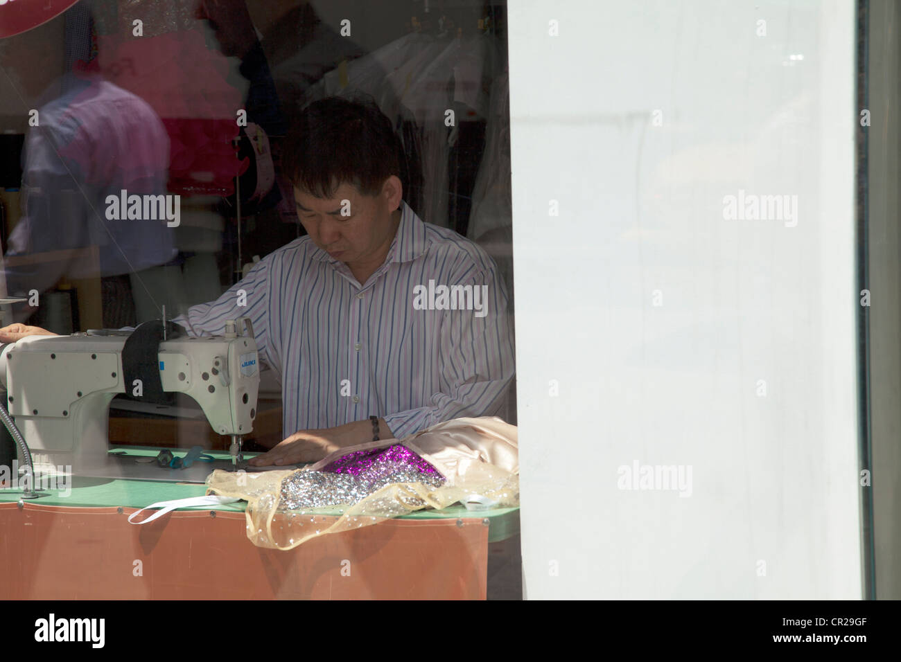 Tailor sewing away on machine in window on street in Manhattan, New