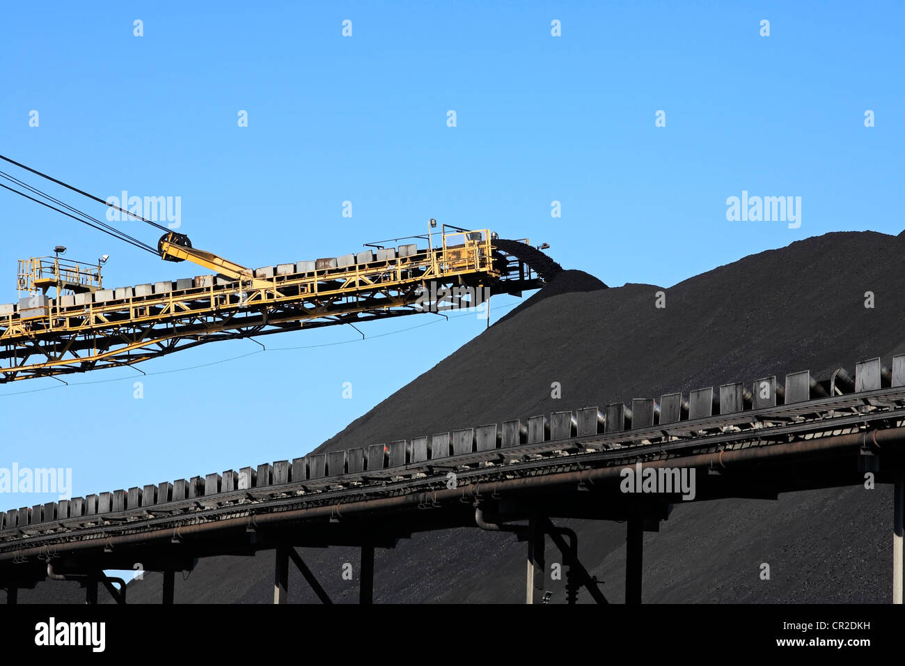 a large yellow conveyor belt carrying coal and emptying onto a huge pile. Stock Photo