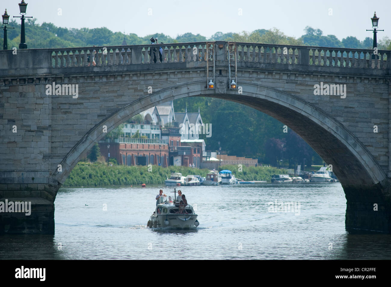 Motor launch travelling downstream on the river Thames under Richmond Bridge, Richmond upon Thames, London Stock Photo