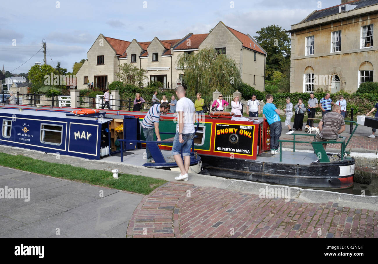 Two narrowboats negotiate Bradford on Avon lock on the Kennet and Avon Canal together, while a crowd of spectators look on. Stock Photo