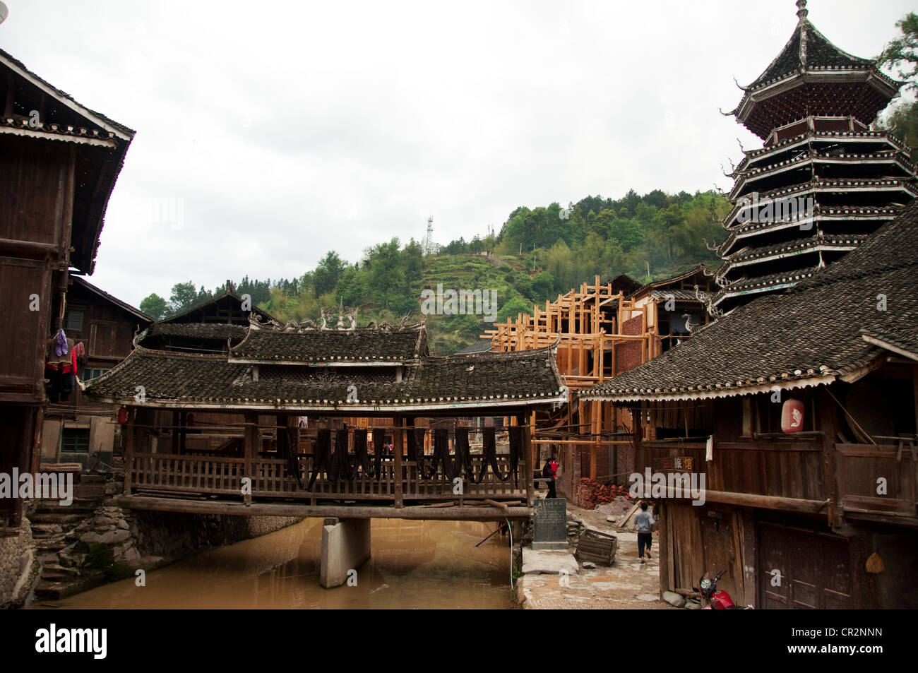 A small 'Wind and Rain' bridge on a water stream and an ancient Drum Tower, Zhaoxing Dong Village, China Stock Photo