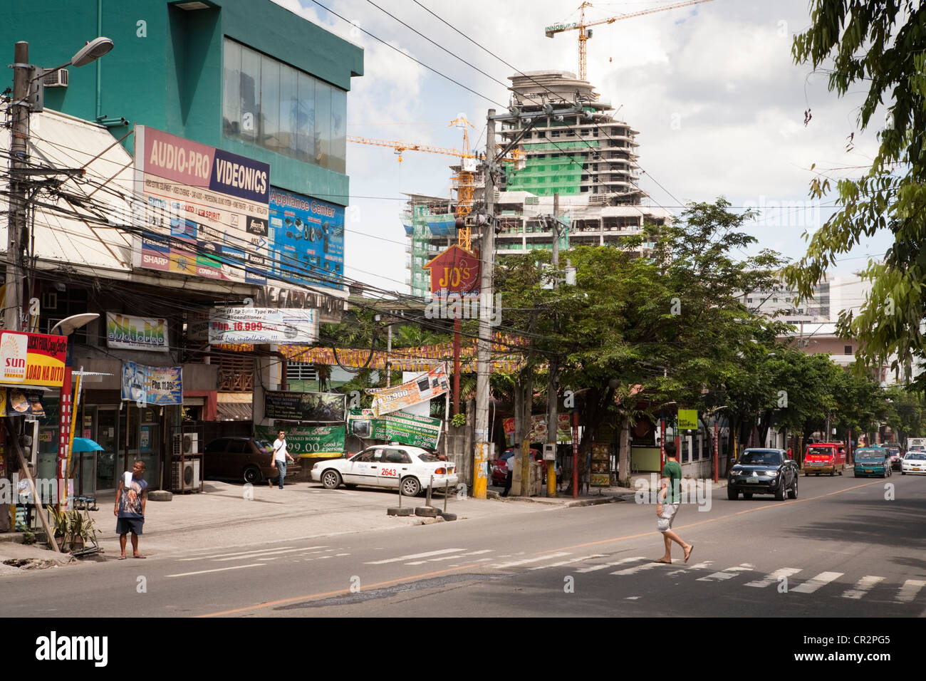 Man crossing the road, the highrise building under construction in the background is part of Asiatown IT Park. Cebu City, Cebu.. Stock Photo