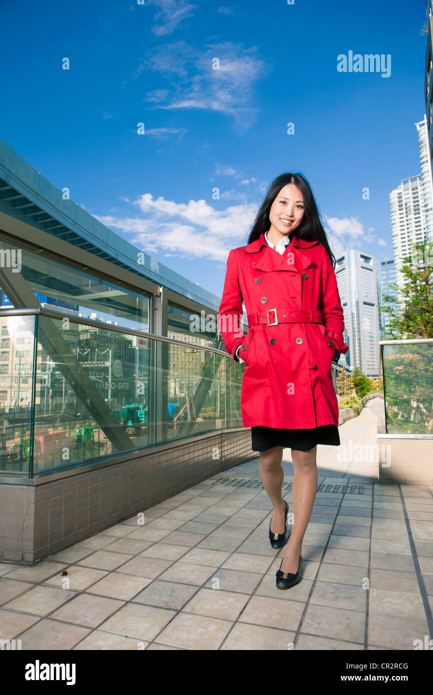 Woman walks along modern city street in red coat Stock Photo