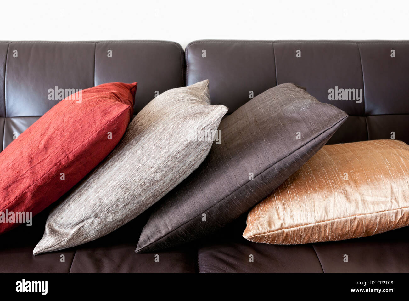 Four Colorful Cushions On Dark Brown Leather Couch Stock Photo