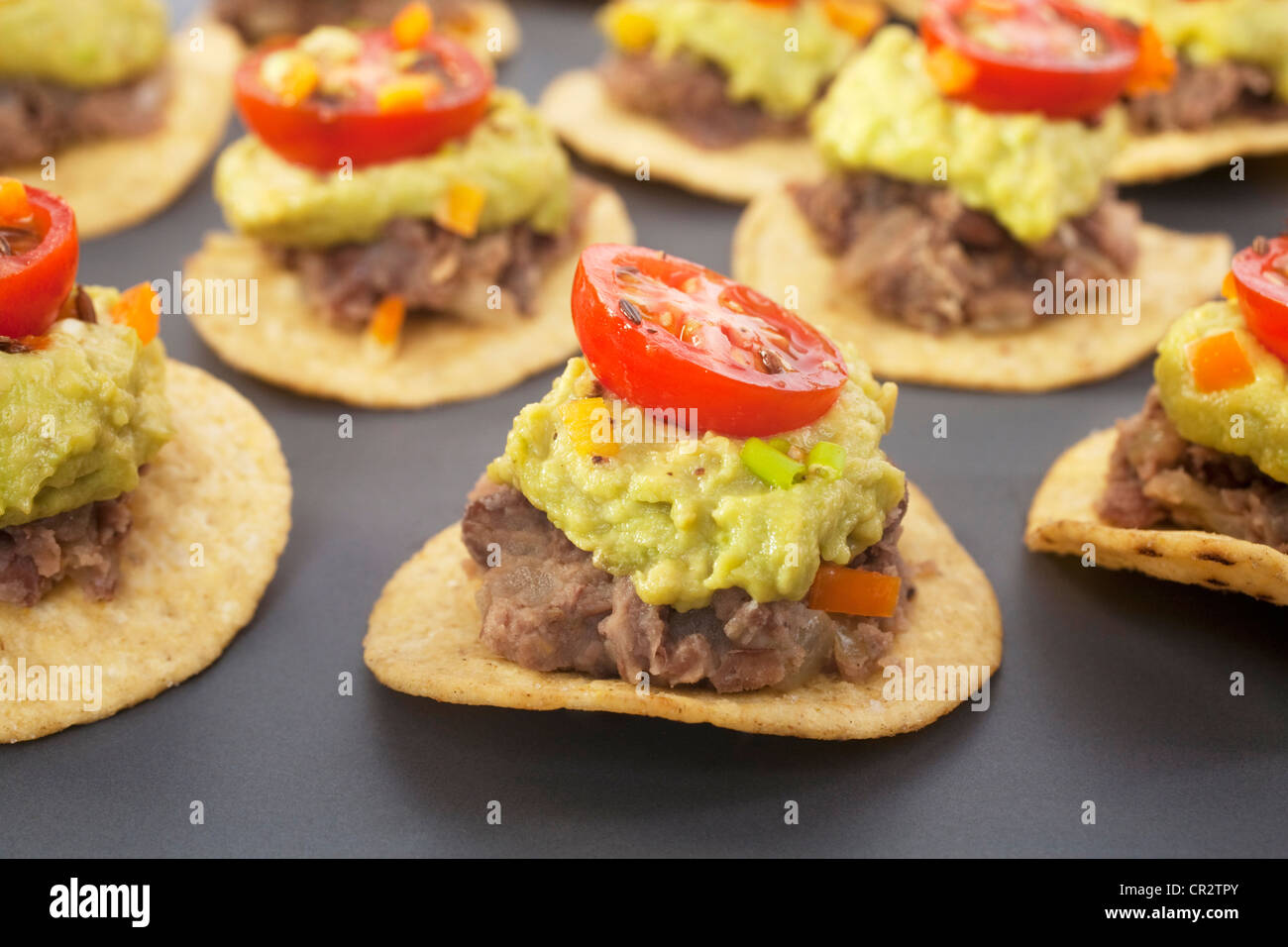 Spicy Mexican party food, corn chips topped with refried beans, avocado and tomato salsa. Stock Photo