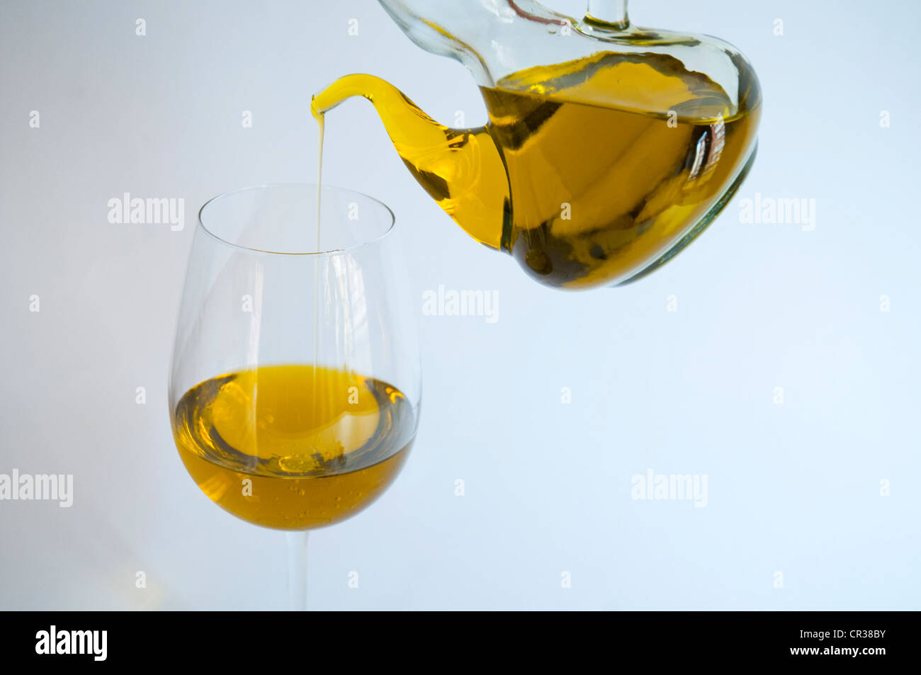 Oil bottle pouring olive oil in a glass. Close view. Stock Photo