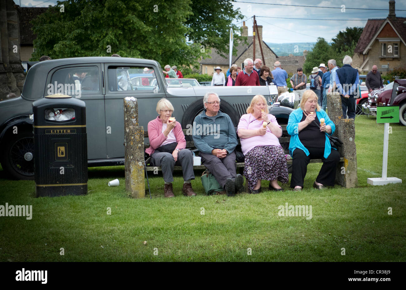 family sitting on a bench eating Ice Cream at a Classic Car event in rural Oxfordshire Stock Photo