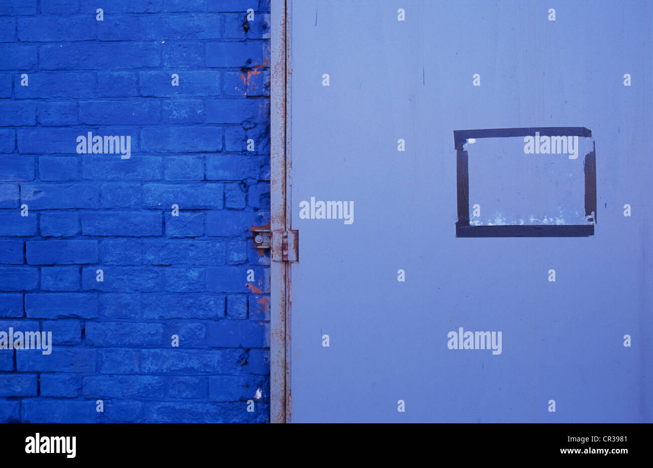 Detail of brick wall painted blue with heavy metal door painted grey and taped rectangle where notice had been Stock Photo