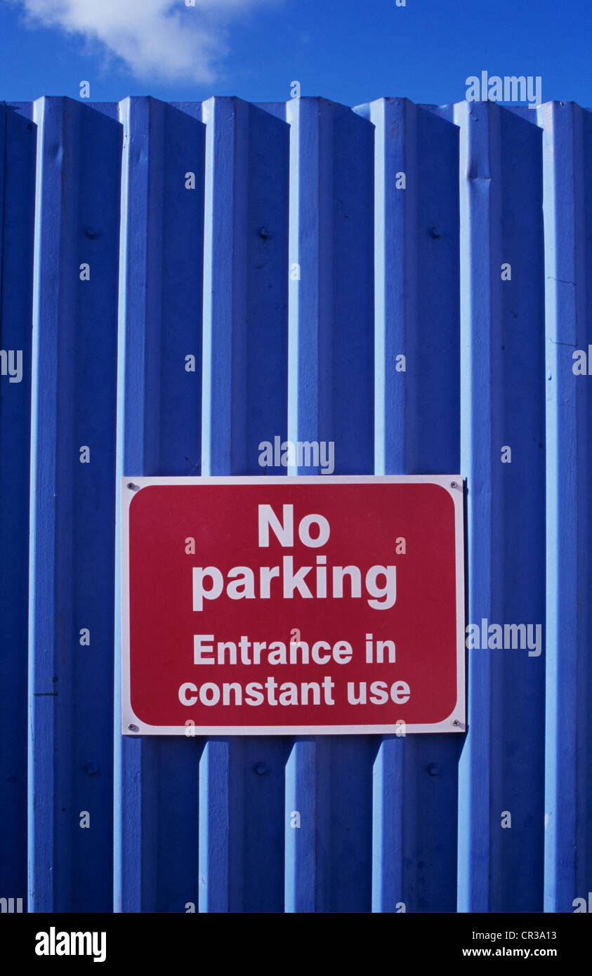 Red and white notice fixed to grey corrugated metal fence or gate stating No Parking Entrance in Constant Use Stock Photo