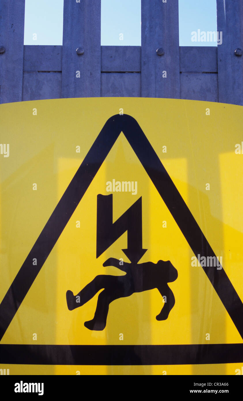 Yellow and black warning sign on heavy duty security fence showing man being struck by electrical thunderbolt Stock Photo