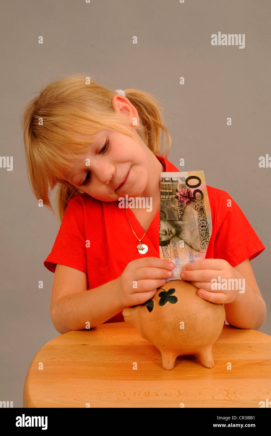 Little girl, 5 years, putting money into a piggy bank Stock Photo - Alamy