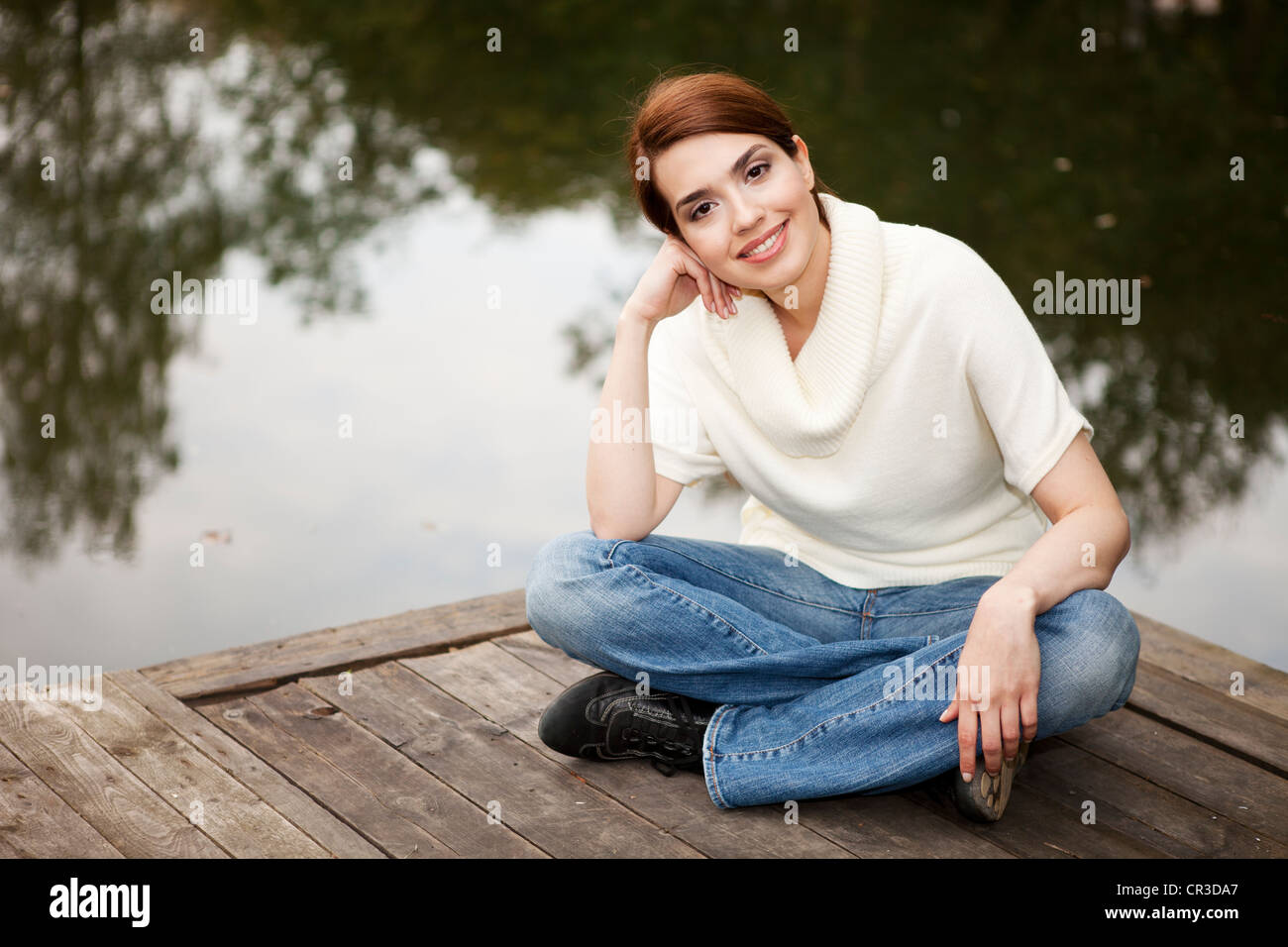 Friendly young smiling woman sitting on a jetty by a lake Stock Photo ...