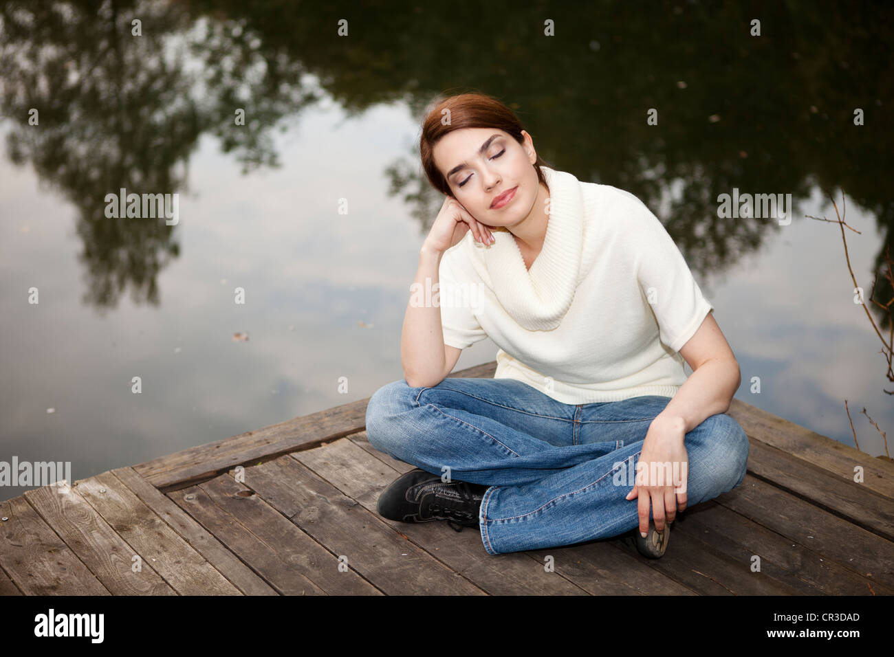 Young woman with closed eyes sitting on a jetty by a lake Stock Photo ...