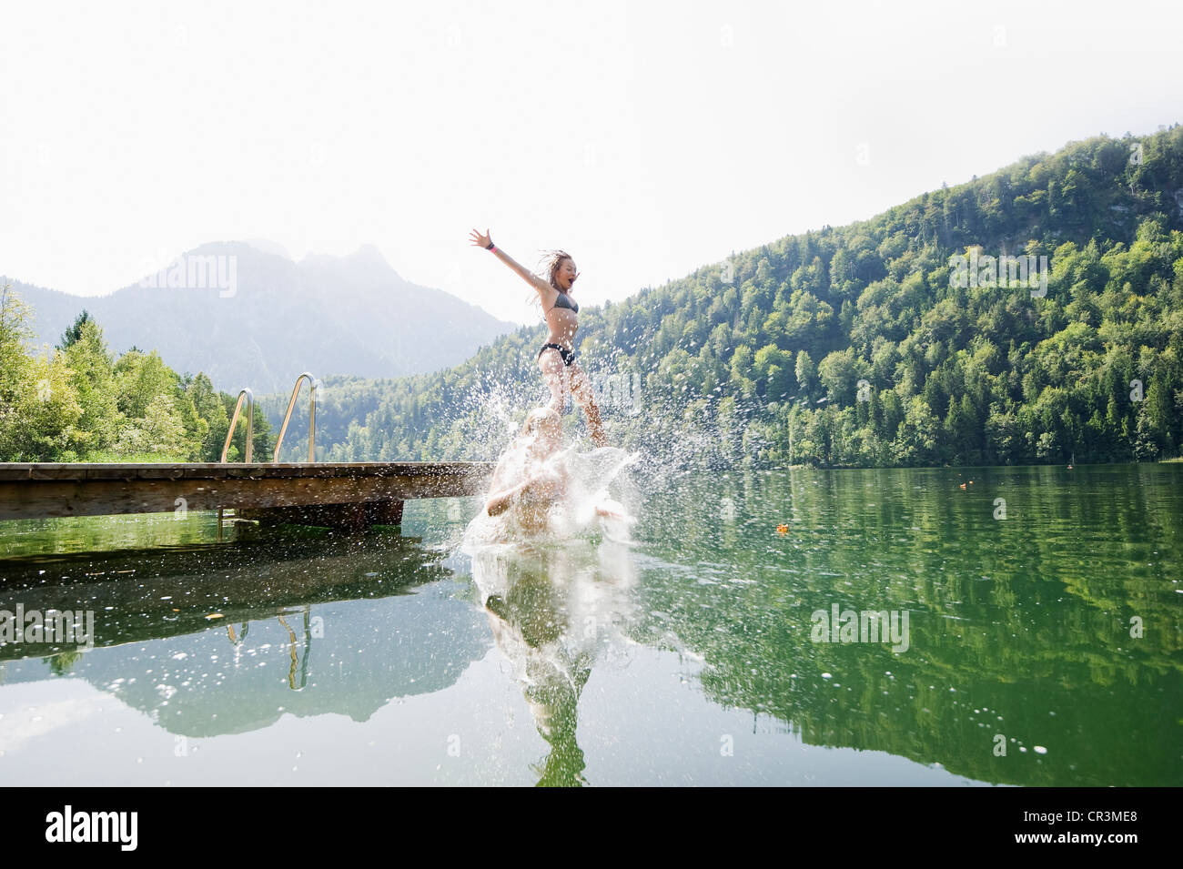 Young women jumping into Schwansee Lake near Fuessen, Allgaeu, Bavaria, Germany, Europe Stock Photo