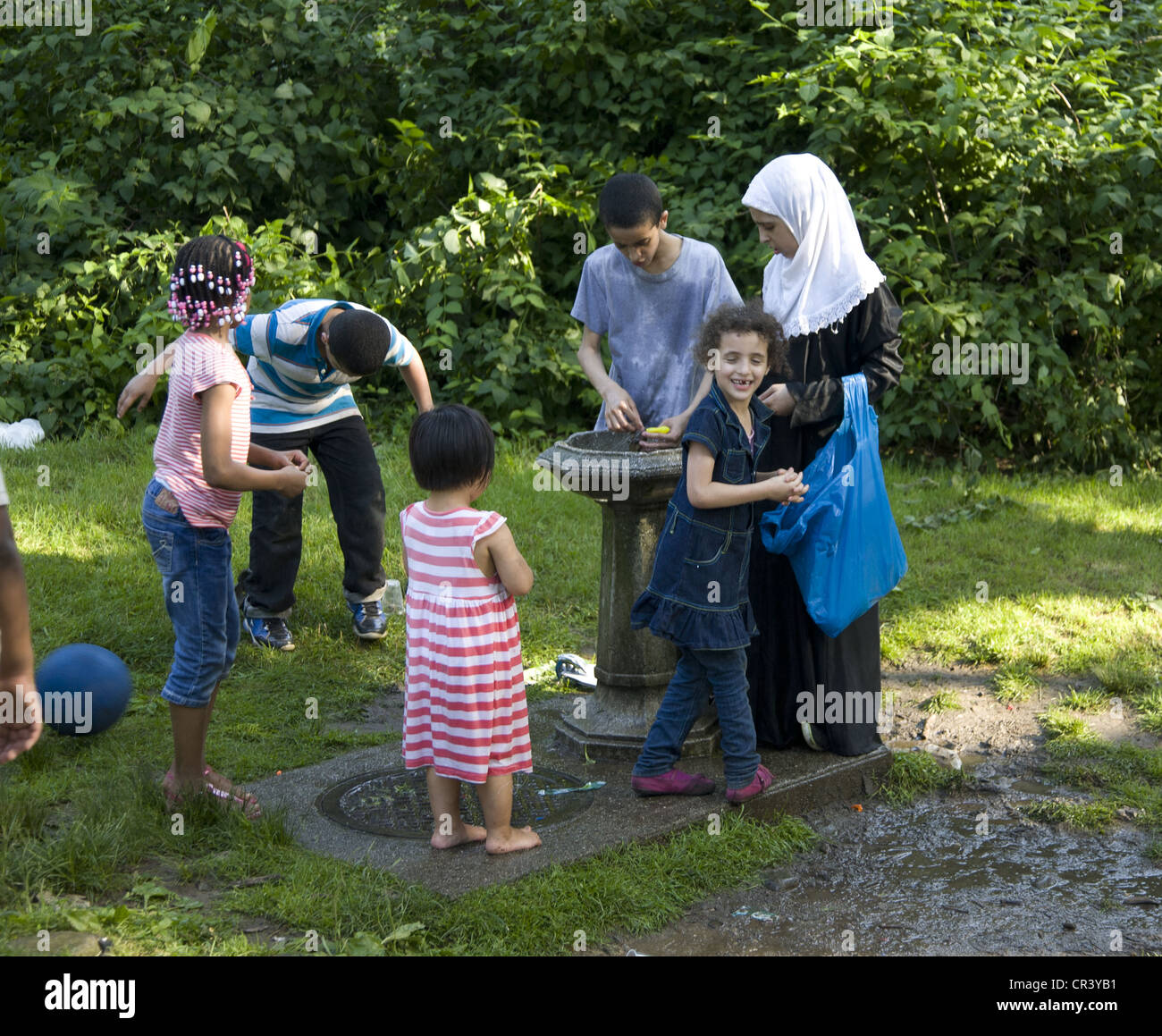 Multiethnic group of children congregate around a water fountain in Prospect Park, Brooklyn, NY on a warm spring day. Stock Photo