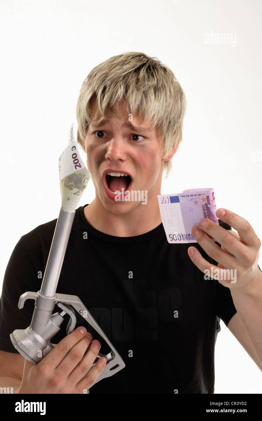 Young man with a desperate expression holding a fuel nozzle with a Euro bill in one hand, in the other hand also a Euro bill, Stock Photo