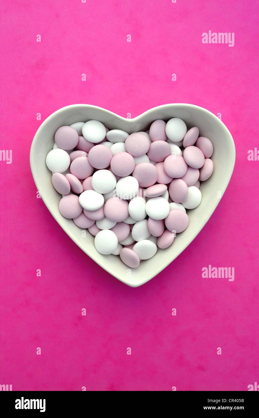 Chocolate beans, chocolate dragees with sugar coating, in heart-shaped porcelain bowl Stock Photo