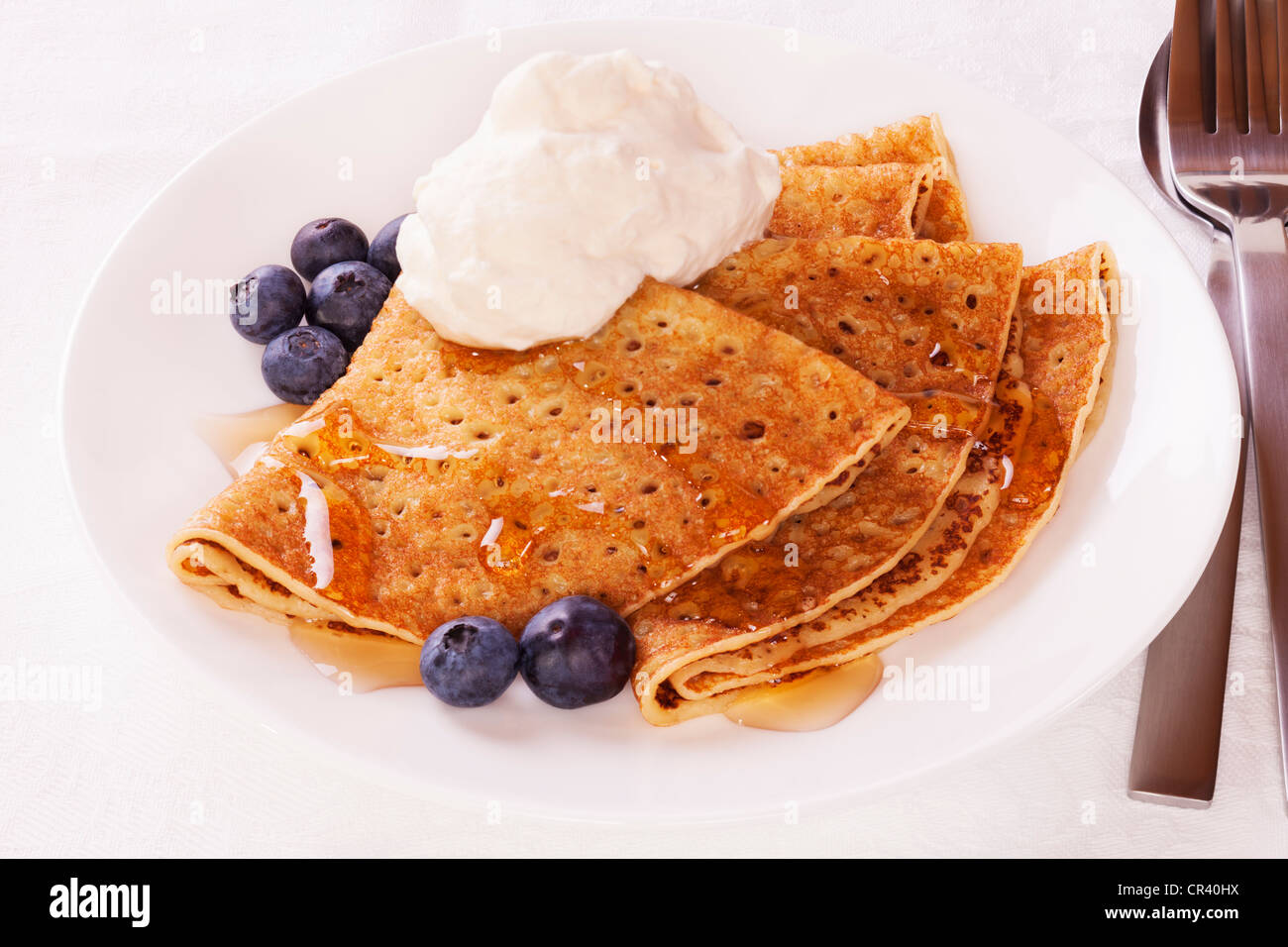 Delicious pancakes or crepes with blueberries, maple syrup and a dollop of whipped cream. Stock Photo