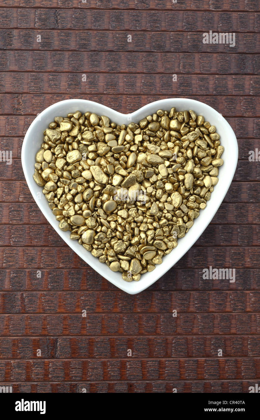 Gold nuggets, precious metal, in heart-shaped porcelain bowl Stock Photo