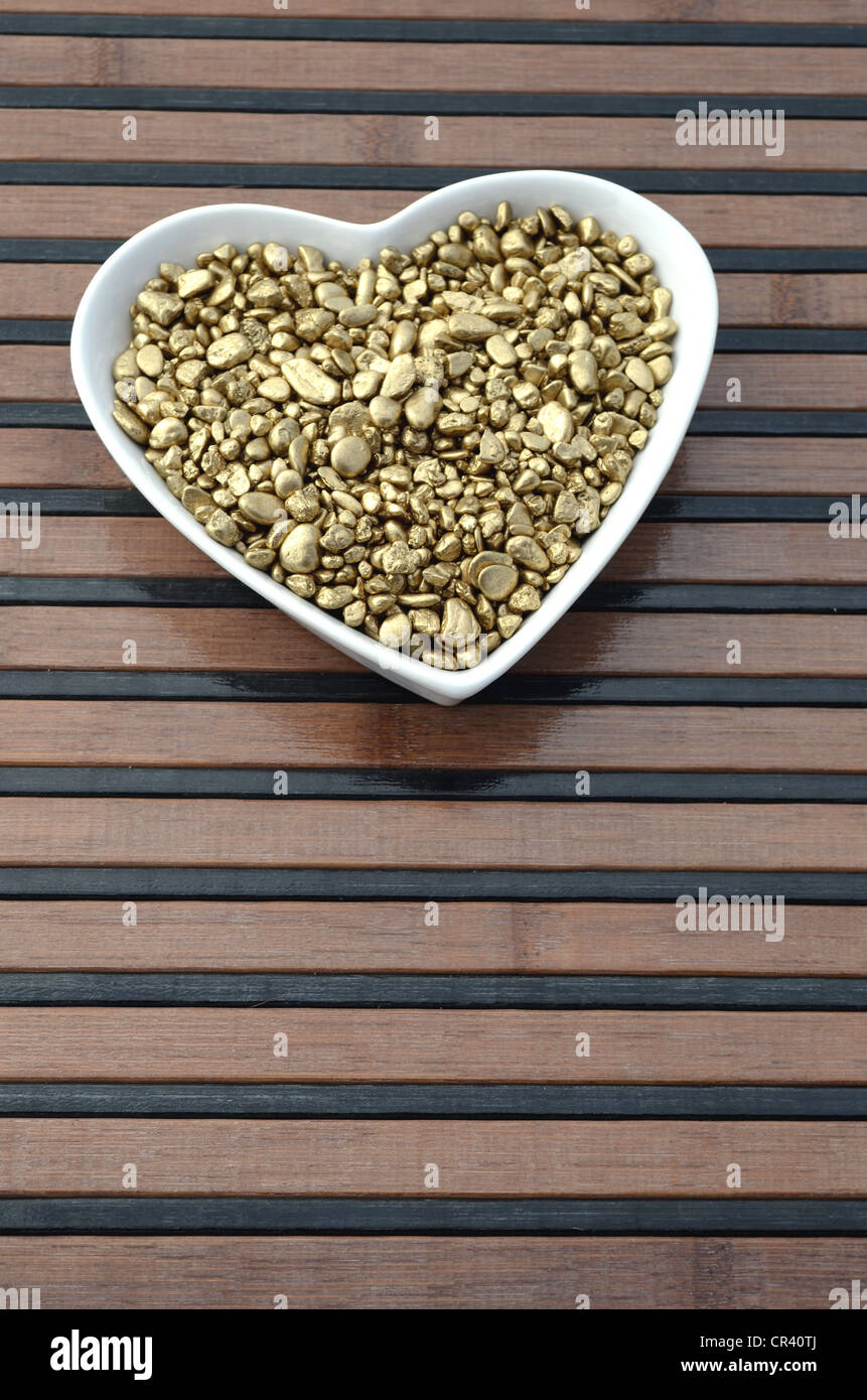 Gold nuggets, precious metal, in heart-shaped porcelain bowl Stock Photo