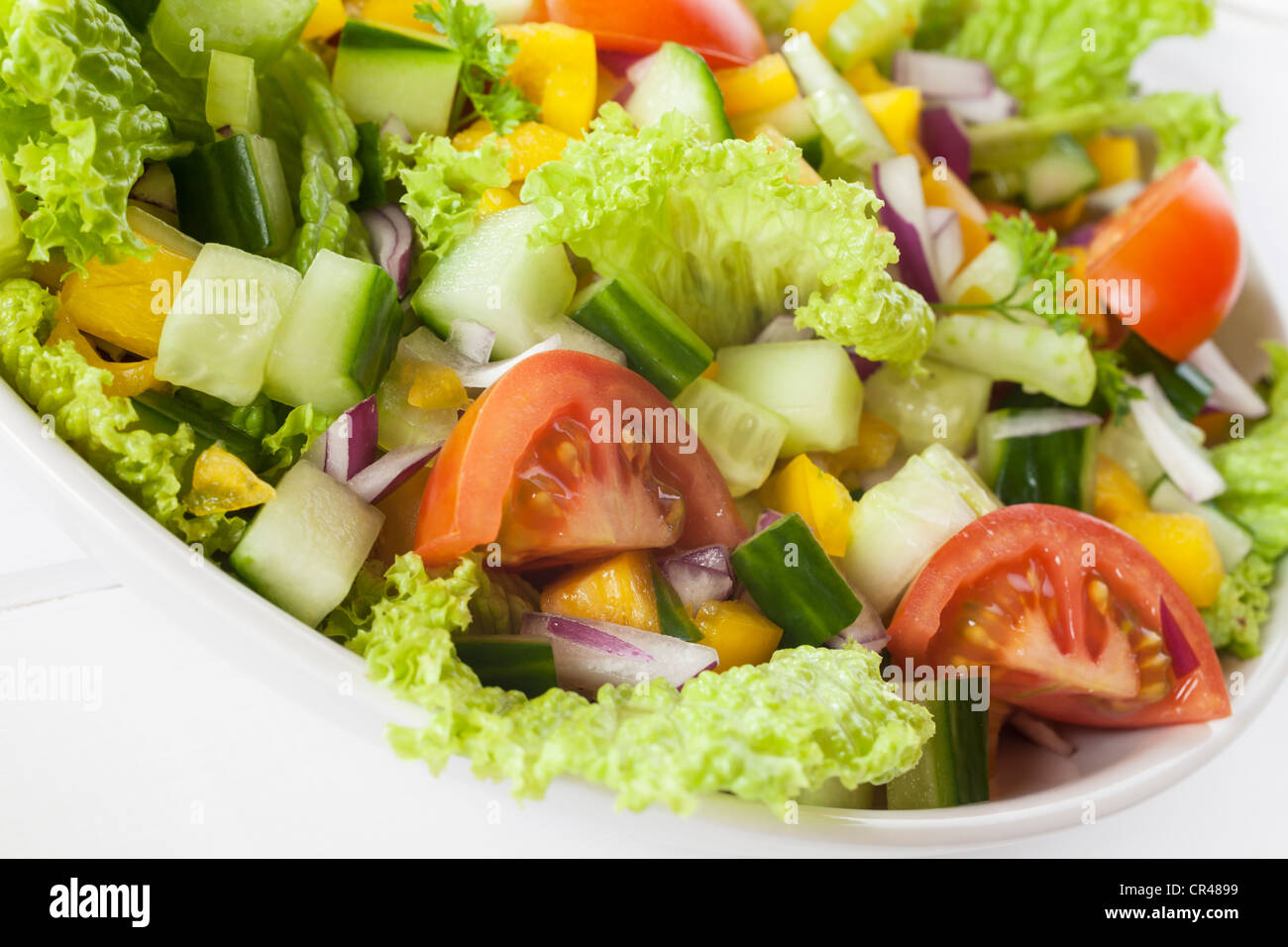A bowl of fresh mixed salad, with lettuce, cucumber, tomato, red onion, yellow capsicum,celery, parsley. Stock Photo