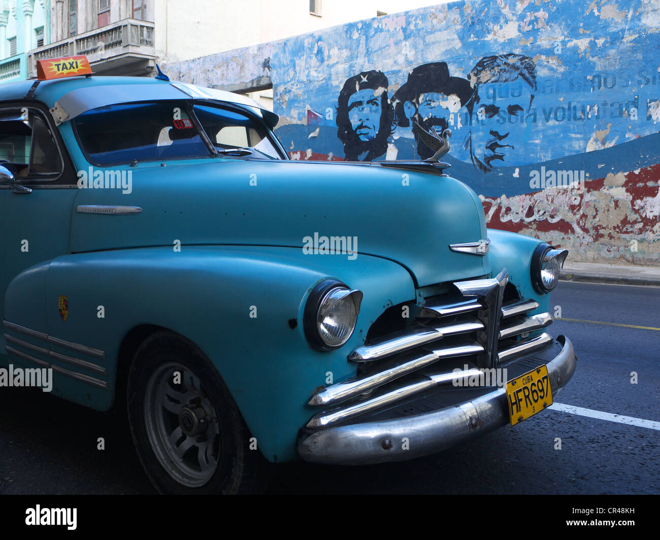American vintage cars as a Cuban taxi driving along a wall with paintings of Fidel Castro and Che Guevara, Havana, Cuba Stock Photo