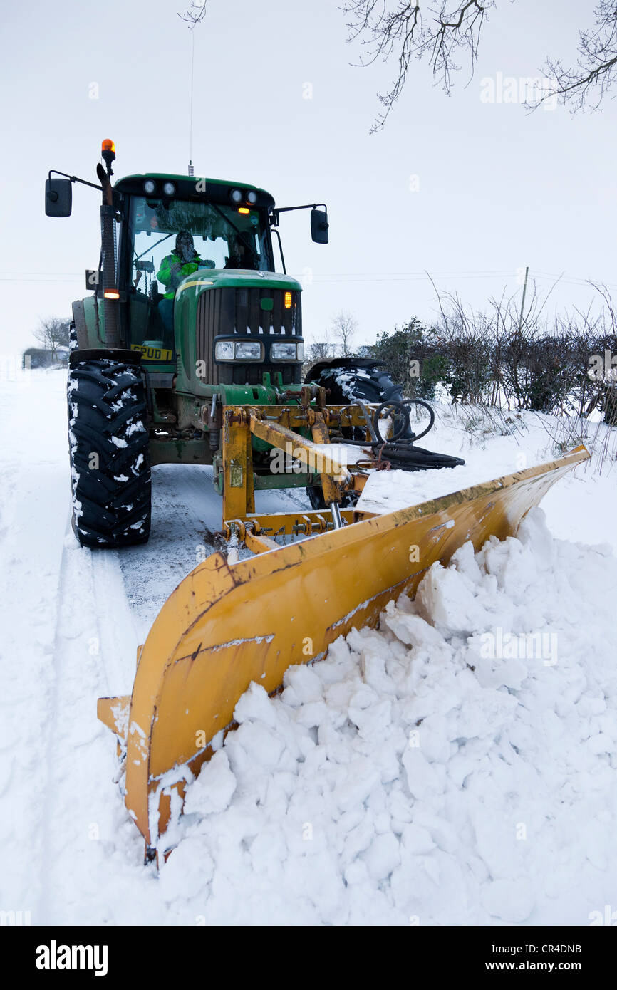A tractor fitted with a front mounted snow plough clearing a road of