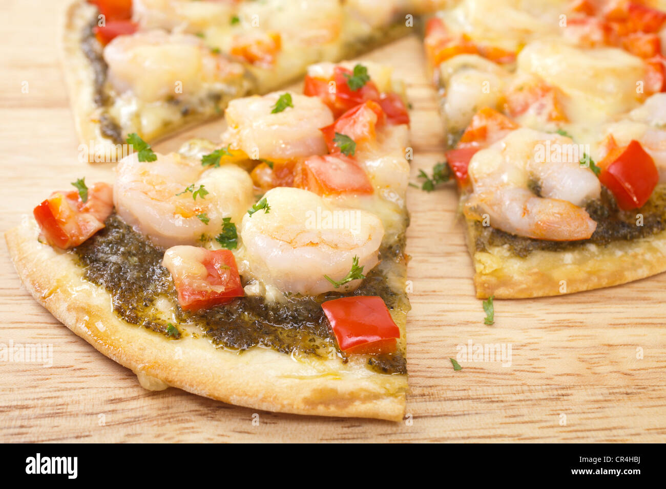 Crispy based pizza topped with prawns, red pepper, mozzarella and basil pesto. Stock Photo