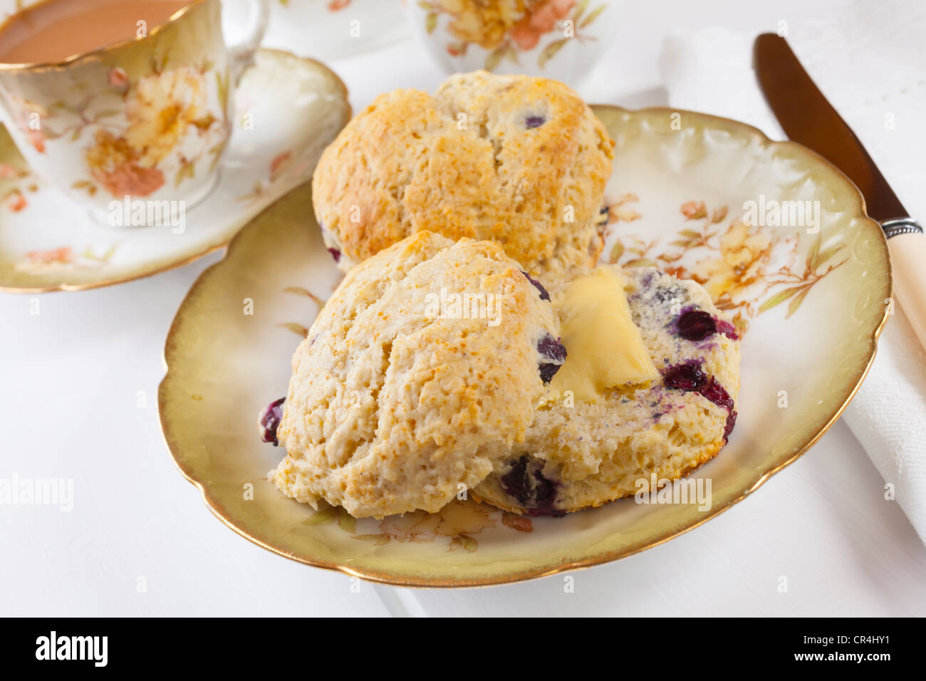 Two blueberry scones with butter and a cup of tea, arranged on beautiful old crockery. Stock Photo