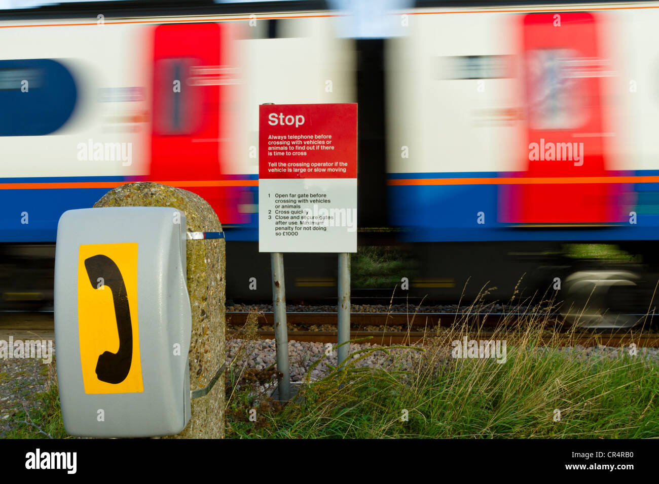 Phone and Stop sign warning of danger at an unprotected railway level crossing with a fast train passing by, Nottinghamshire, England, UK Stock Photo