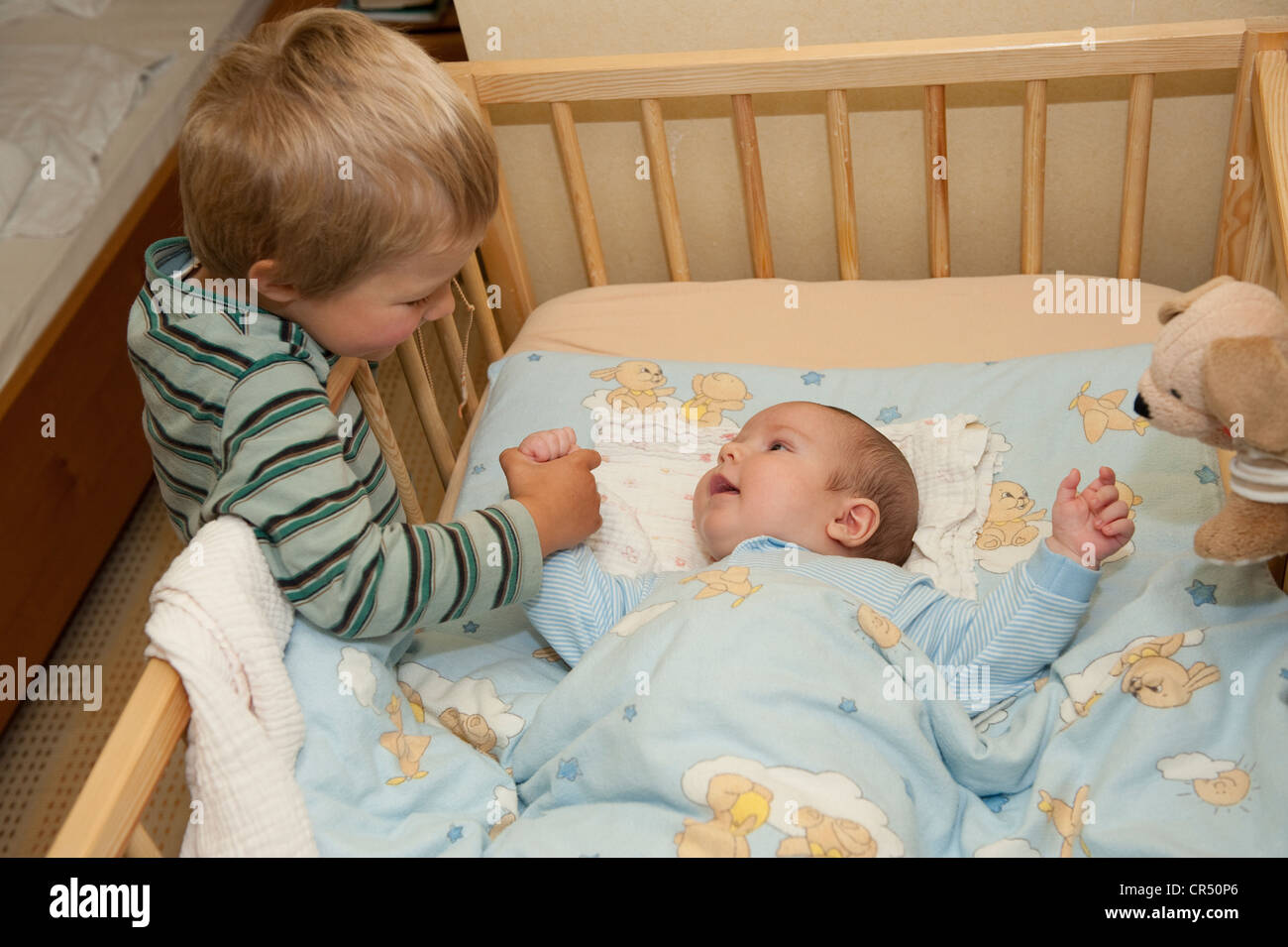 Boy, 3 years, playing with his little brother, 4 months, at the crib, holding his hand Stock Photo
