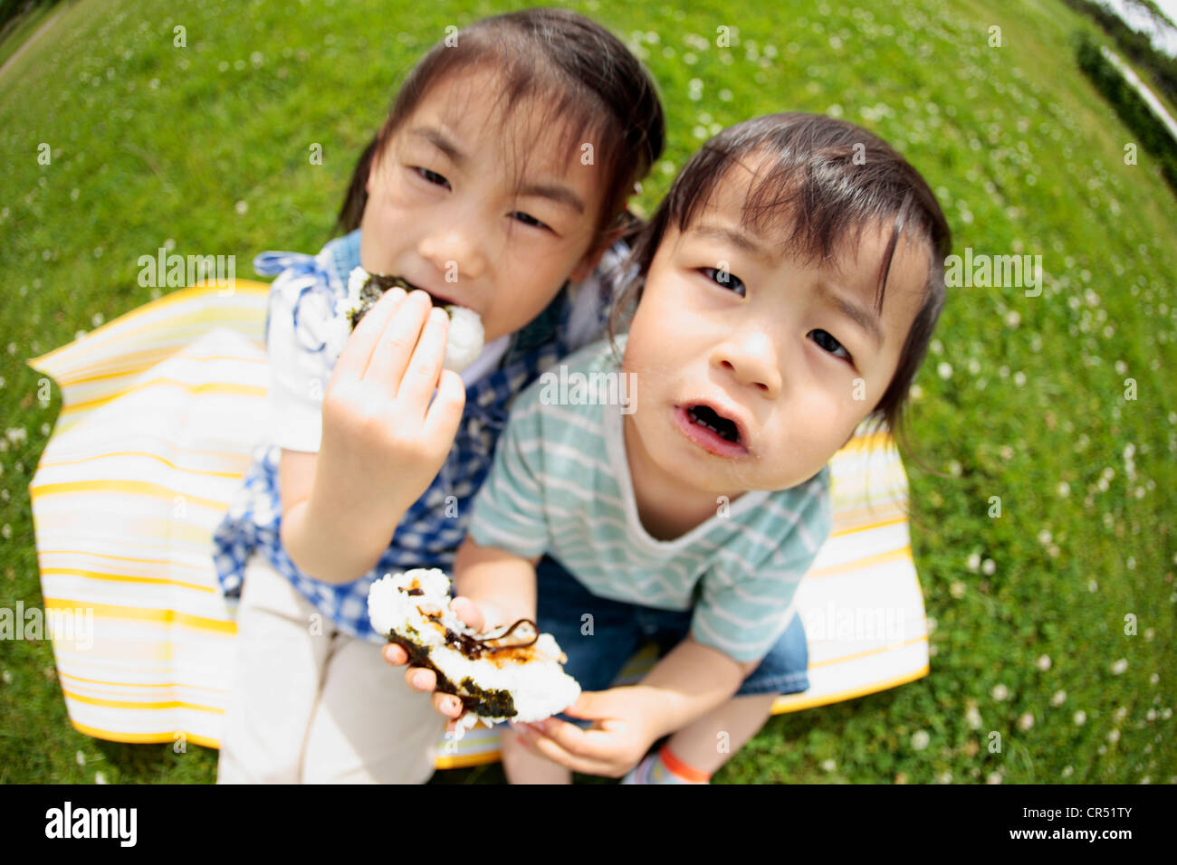 Girl and Boy Sitting on Grass and Eating Rice Ball Stock Photo - Alamy