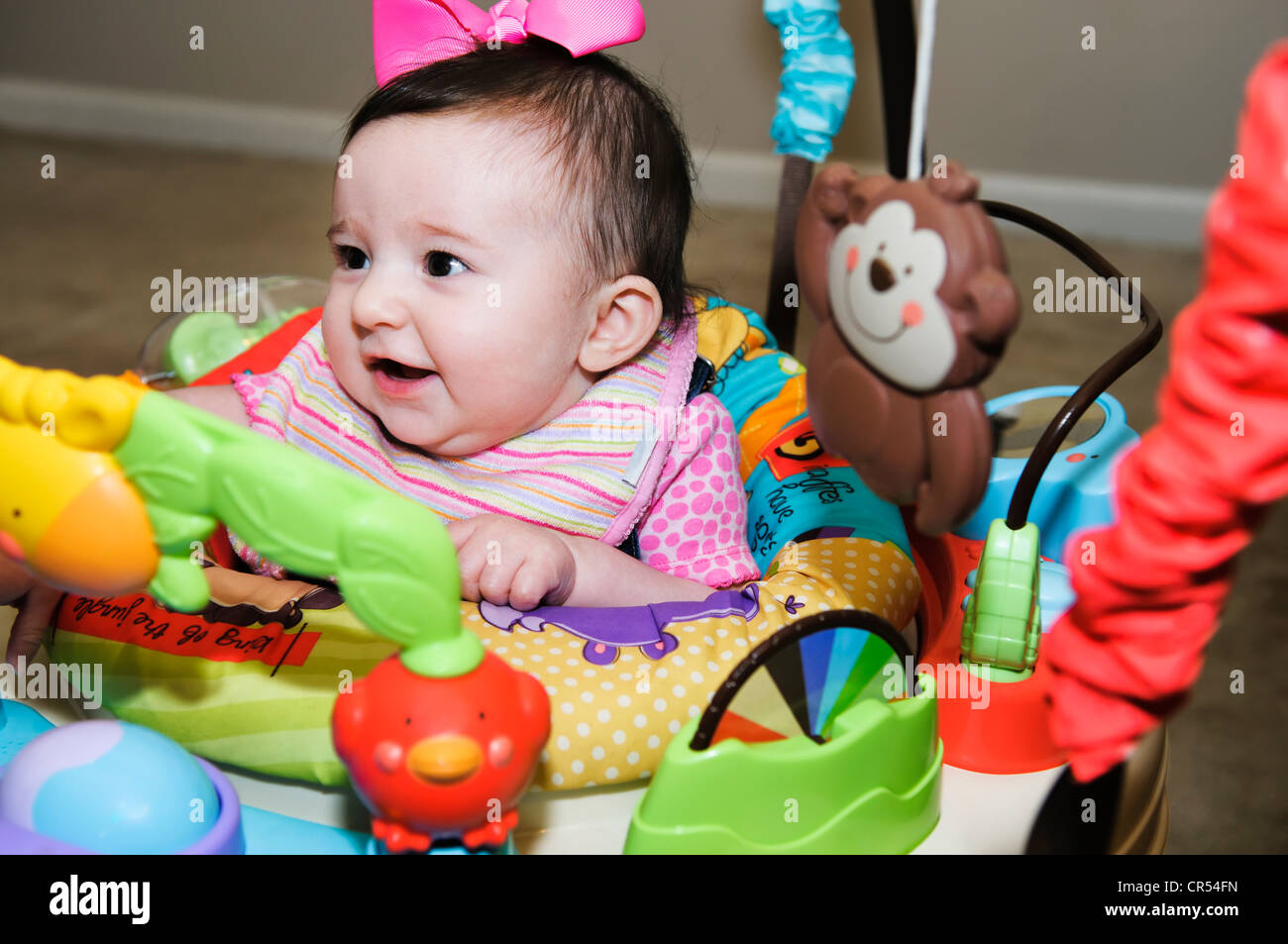 Adorable baby girl is entertained while playing in her padded educational jumper seat surrounded by interactive toys. Stock Photo