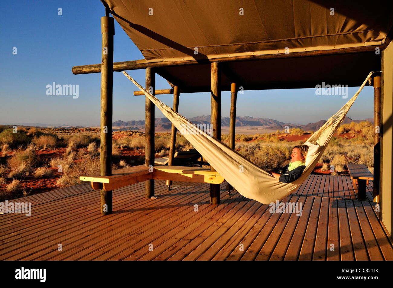 Tourist in a hammock in front of a chalet of the Wolwedans Dune Lodge in the Namib Rand Nature Reserve, Namib Desert, Namibia Stock Photo