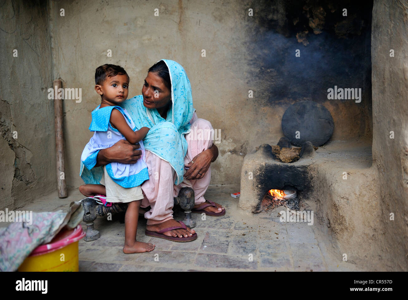 Woman holding her daughter in her arms while cooking with a simple clay oven, she lives and works with her family under the Stock Photo