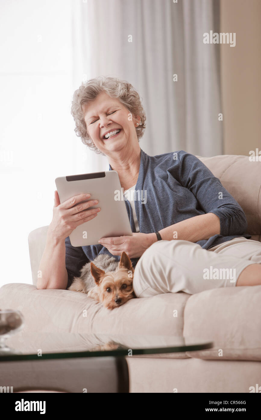 Caucasian woman sitting on sofa using digital tablet with dog Stock Photo