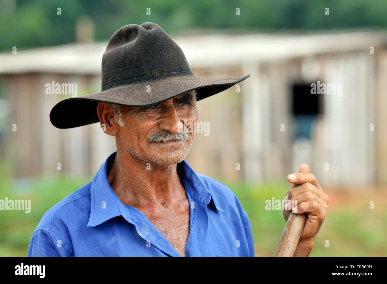 https://c8.alamy.com/comp/CR569N/farmer-wearing-a-hat-standing-in-front-of-his-hut-acampamento-12-de-CR569N.jpg