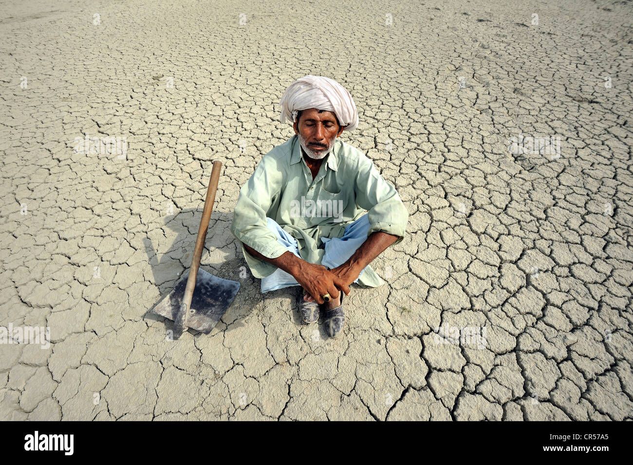Farmer with closed eyes sitting on dried loamy soil, dreaming, Basti Lehar Walla village, Punjab, Pakistan, Asia Stock Photo
