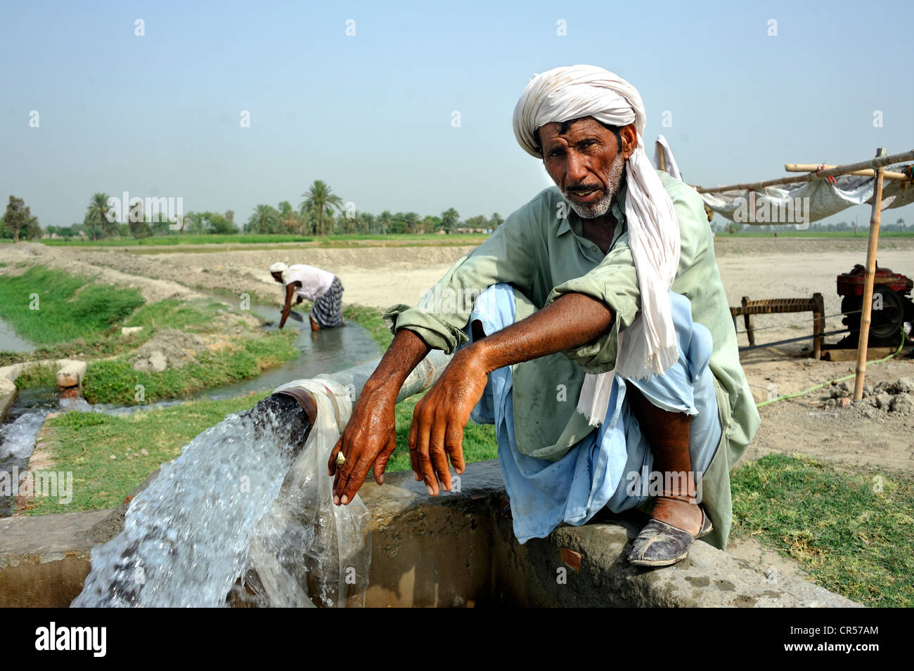 Farmer squatting on the catchment of a spring that is feeding an agricultural irrigation canal, Basti Lehar Walla village, Stock Photo