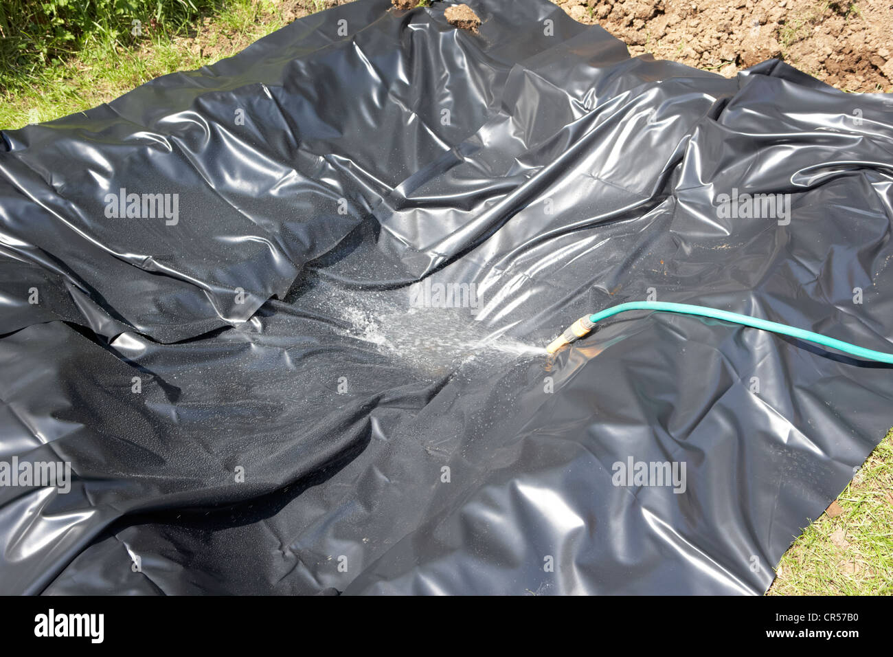 using a hose to fill a hole lined with a pond liner to create a pond in a garden in the uk Stock Photo