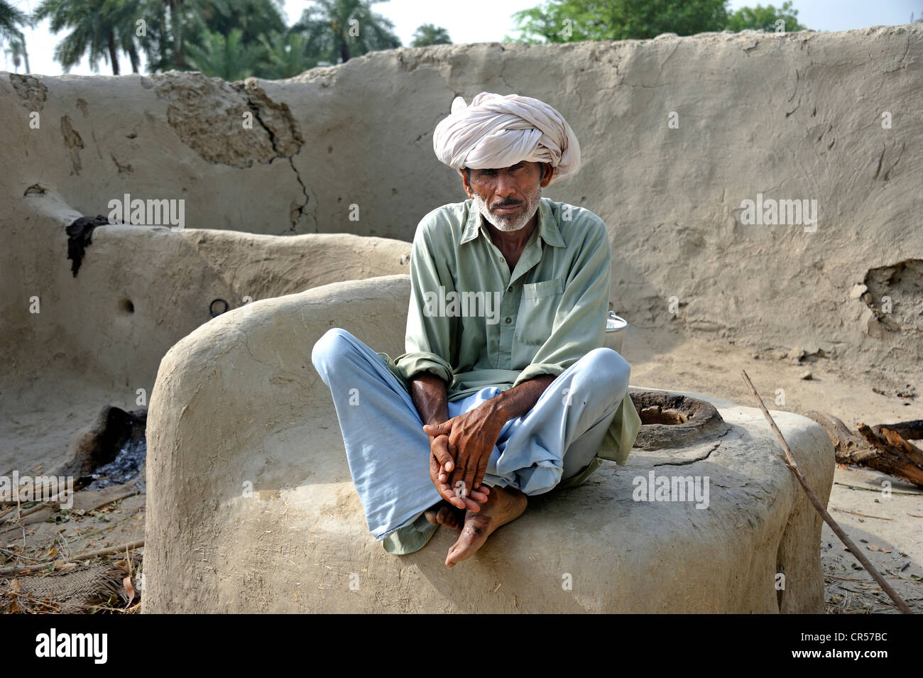 Elderly man wearing a turban is sitting on a bread oven, Basti Lehar Walla village, Pubjab, Pakistan, Asia Stock Photo