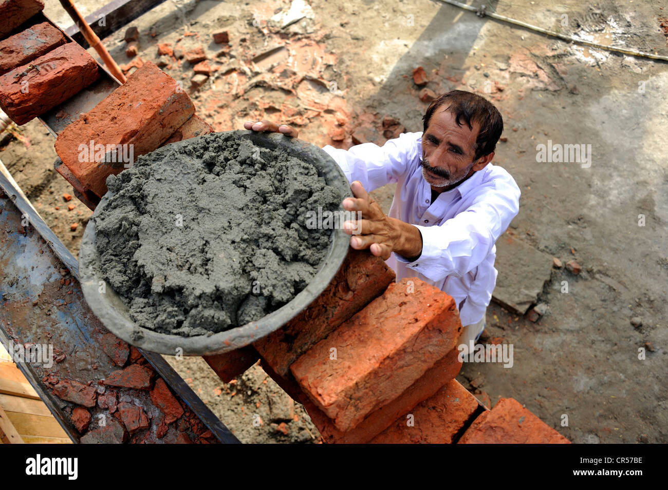 Man lifting pan with cement onto a scaffold, construction of brick