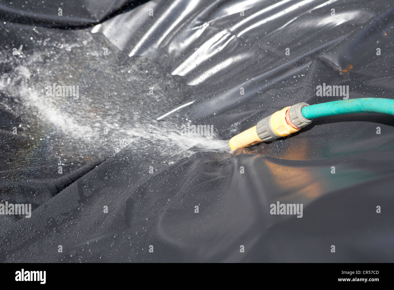using a hose to fill a hole lined with a pond liner to create a pond in a garden in the uk Stock Photo